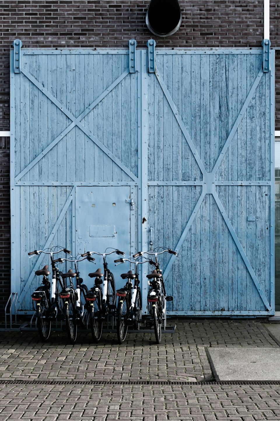 Fem cyklar parkerade i ett ställ framför en sliten blå grind.